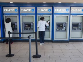 In this March 24, 2020 file photo, a Chase bank employee, right, cleans the branch's ATMs as a customer uses another in the Flushing neighbourhood of the Queens borough of New York City.