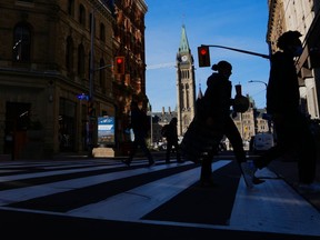 The Canada Flag flies on the Peace Tower of Parliament Hill as pedestrians make their way along Sparks Street Mall in Ottawa, Nov. 9, 2021. Federal public servants are expected to be back in office by the end of the month.