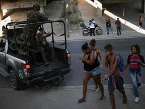 Locals walk past a truck carrying militarized police members during a police operation at the Salgueiro Complex, in Sao Goncalo, Rio de Janeiro state, Brazil, on March 23, 2023.