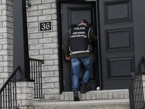 A police officer heads into a home in Blainville on Wednesday, March 29, 2023, as part of an investigation into the Hells Angels.