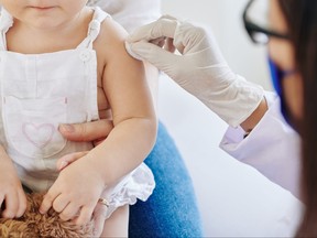 Doctor in rubber gloves wiping injection site on arm of little girl before vaccination.