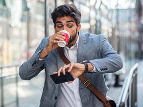 Worried businessman looking at his watch, drinking coffee and running late.