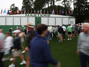 Patrons at Masters Tournament in front of giant leaderboard.