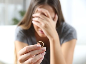 Closeup of a sad woman after divorce holding wedding ring.