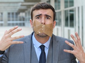 Frustrated businessman with tape covering mouth unable to express his opinion.