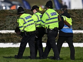 An animal rights protester is taken away by police officers at the second fence ahead of the Grand National Handicap Steeple Chase on the final day of the Grand National Festival horse race meeting at Aintree Racecourse in Liverpool, England, Saturday, April 15, 2023.