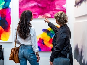 Backs of two women looking at artworks on wall.