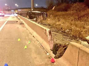 Smashed concrete wall on highway with flipped over car in background