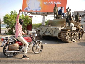 A man raises his arm in support as he drives near Sudanese army soldiers loyal to army chief Abdel Fattah al-Burhan, manning a position in the Red Sea city of Port Sudan, on April 20, 2023.