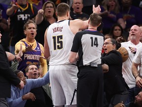 Nikola Jokic of the Denver Nuggets reaches for the basketball after pushing off Phoenix Suns owner Mat Ishbia (seated at left) during Sunday's game.