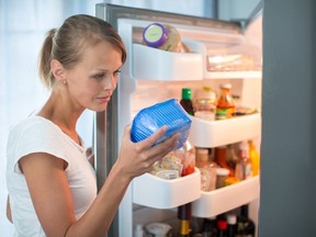 Is this still fine? Pretty, young woman in her kitchen by the fridge, looking at the expiry date of a product she took from her fridge -