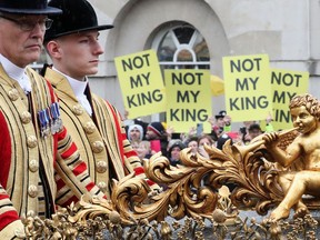 A coach carrying Prince William, Catherine, Princess of Wales and their children Prince George, Princess Charlotte and Prince Louis rides past anti-monarchy protesters following the coronation ceremony for King Charles III and Queen Camilla.