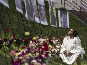 Simone Crawley kneels as she looks up at a photograph of her grandmother, Ruth Whitfield, among a display of victims of last year's racist massacre at a Buffalo supermarket during the 5/14 Community Gathering for Reflection, Healing, and Hope at the Johnnie B. Wiley Amateur Athletic Sports Pavilion in Buffalo, N.Y. on Saturday, May 13, 2023.