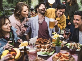 Group of friends laughing, drinking beer and wine and eating together.