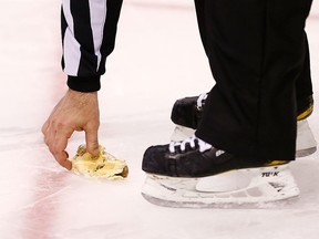 A referee picks up a hot dog off of the ice that was thrown from the stands during the first shootout attempt by Tyler Seguin of the Boston Bruins against the New Jersey Devils during the game on January 29, 2013 at TD Garden in Boston, Massachusetts.  (Photo by Jared Wickerham/Getty Images)