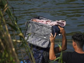 A migrant crosses the Rio Grande river with a baby in a suitcase, as seen from Matamoros, Mexico, Wednesday, May 10, 2023.