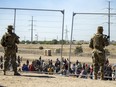 Migrants wait in line adjacent to the border fence under the watch of the Texas National Guard to enter into El Paso, Texas, Wednesday, May 10, 2023.