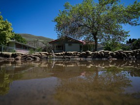 Water is pumped out from a flooded home near the Bonaparte River as sandbags line a sidewalk in Cache Creek, B.C., on May 14, 2023.