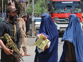 Afghan burqa-clad women walk past a Taliban security personnel along a street in Jalalabad on April 30, 2023.