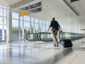In this file photo, a tourist with baggage walks towards a moving walkway at an airport