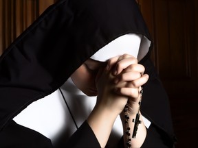 Nun folding hands holding a rosary praying