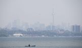 A person in a canoe goes for a paddle on Lake Ontario as smoke from wildfires partly obscures Toronto's skyline at Humber Bay Shores Park on Wednesday, June 7, 2023.