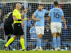 Referee Szymon Marciniak shows a yellow card to Manchester City's Ruben Dias, center, during the Champions League semifinal second leg soccer match between Manchester City and Real Madrid at Etihad stadium in Manchester, England, Wednesday, May 17, 2023.