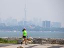 Winnie Wong walks her dog at Humber Bay Shores Park on June 7, 2023, as a haze obscures the view of the Toronto skyline. (Ernest Doroszuk, Toronto Sun)