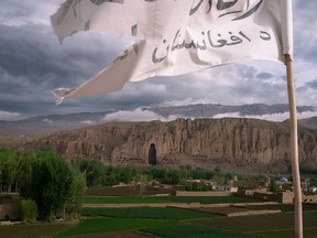A tattered Taliban flag flies from the roof of a hotel in Bamian, Afghanistan. The recesses that once sheltered giant figures of the Buddha can be seen in the cliff face beyond.