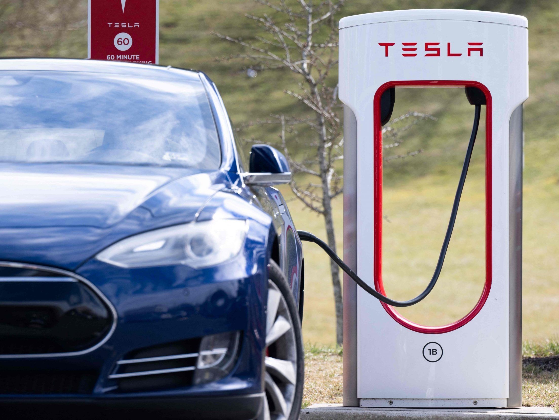 A Tesla Model S sedan is plugged into a Tesla Supercharger electrical vehicle charging station