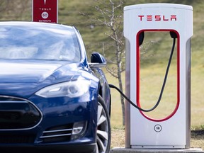 A Tesla Model S sedan is plugged into a Tesla Supercharger electrical vehicle charging station