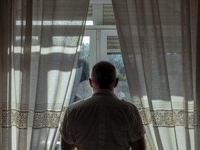 Rear view of adult man standing beside window with sunlight and shadow