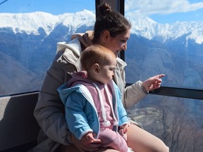 Woman with toddler daughter looks at mountain landscape from cable-way cabin.