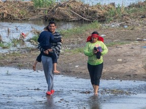 Migrants walk in the water along the Rio Grande border with Mexico in Eagle Pass, Texas, Sunday, July 16, 2023.