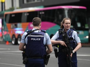 Armed New Zealand police officers stand outside of a hotel.