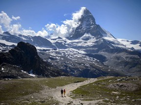 A couple of tourists walk on a trail below the Matterhorn