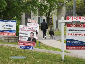 A person walks past multiple for-sale and sold real estate signs in Mississauga, Ont.
