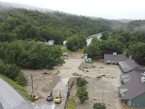 construction vehicles stand by as muck, mud and floodwater block a section of Route 203 in Ludlow, Vt.