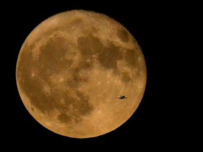 A commercial airliner flies Northwest across Lake Michigan in front of the "Full Buck" supermoon, the first of four supermoons in 2023, July 3, 2023, in Chicago.