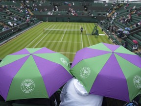 People sit under umbrellas as rain delays the start of play on day three of the Wimbledon