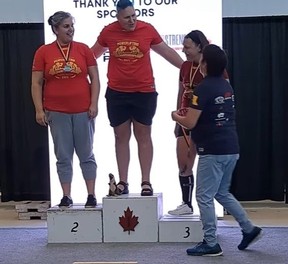Anne Andres (centre) stands on the podium with a T-Rex toy at her feet after winning the 2023 Western Canadian Championship.
