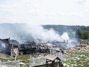 Two firefighters stand on the debris around the smoldering wreckage of the the three houses that exploded near Rustic Ridge Drive and Brookside Drive in Plum, Pa., on Saturday, Aug. 12, 2023.