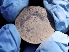 This photo, provided by the U.S. Military Academy at West Point, Aug. 30, 2023, shows West Point archeologist Paul Hudson display an 1828 Capped Bust Half Dollar, one of the coins found in the lead box believed to have been placed in the base of a monument by cadets almost two centuries ago, in West Point, N.Y.