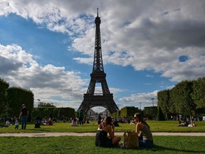 Tourists and Parisians sit in the Champ de Mars in front of the Eiffel Tower in Paris on August 9, 2023