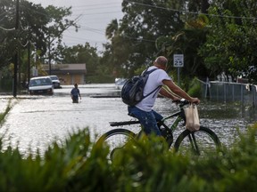 A cyclist looks on as Dani Araus, 27, walks down a flooded street at Palmetto Beach in Tampa, Fla., as Hurricane Idalia approaches the Big Bend region on Wednesday, Aug. 30, 2023.