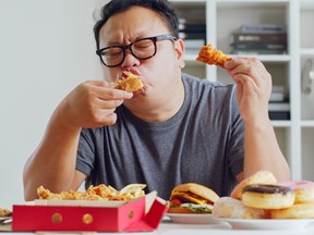 A man enjoys a meal of junk food, including a hamburger, pizza and fried chicken
