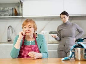 Elderly sad woman stands in kitchen and listens