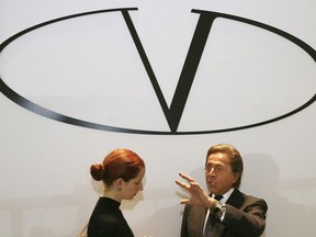 FILE - Italian fashion designer Valentino, right, standing underneath the logo of his fashion house, answers the questions of a fashion reporter prior to the presentation of his Haute Couture Spring-Summer 2008 fashion collection, on Jan. 23, 2008, in Paris. French luxury conglomerate Kering has reached a cash deal to purchase a 30% stake in Italian fashion house Valentino for 1.7 billion euros from a Qatari investment firm.