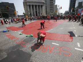 Family and supporters paint a red dress in Winnipeg on Thursday, Aug. 3, 2023, as they gathered to protest the lack of action from all levels of governments in funding a search of a landfill for missing Indigenous women.