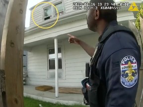 A police officer points to a second floor window at a house